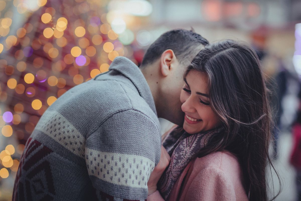 Un couple s'embrasse tendrement dans la rue, avec des lumières de fête floues en arrière-plan
