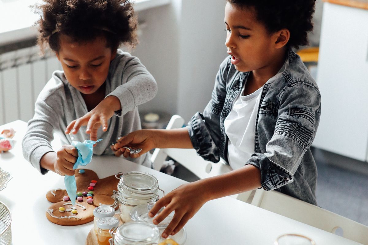 Deux enfants qui décorent des biscuits de Noël à une table de cuisine claire