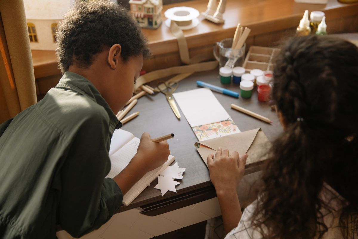 Deux enfants penchés sur une table de bricolage, en train d'écrire une lettre de Noël
