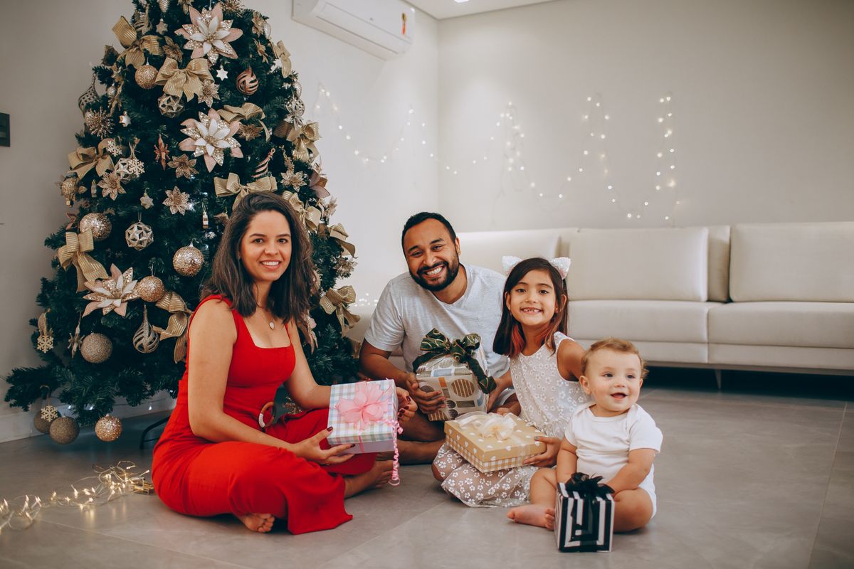 Famille réunie sur le tapis d'un salon devant un sapin de Noël décoré : une femme en robe rouge, un homme et deux jeunes enfants