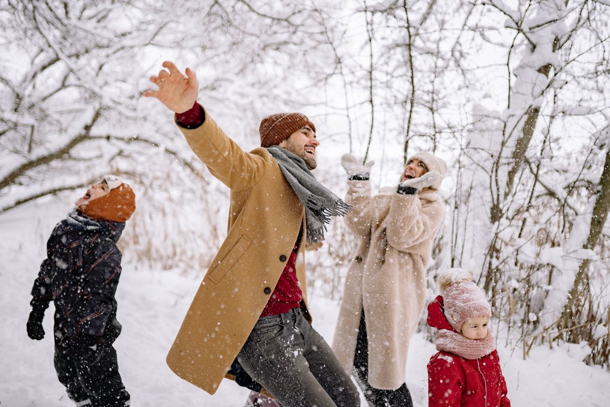 Parents et enfants en manteaux, bonnets et écharpes qui jouent dans la neige, au milieu d'arbres givrés