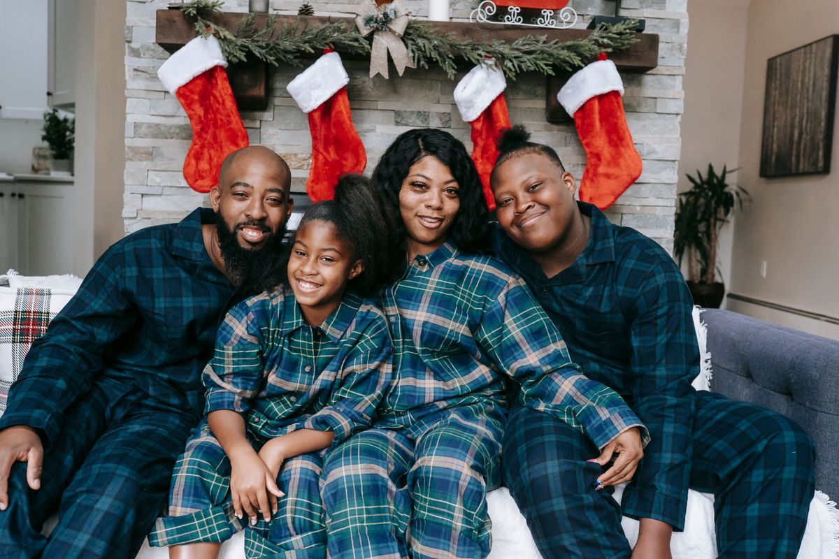 Famille en pyjamas de Noël à carreaux assortis, installée sur un canapé devant une cheminée ornée de chaussettes rouges